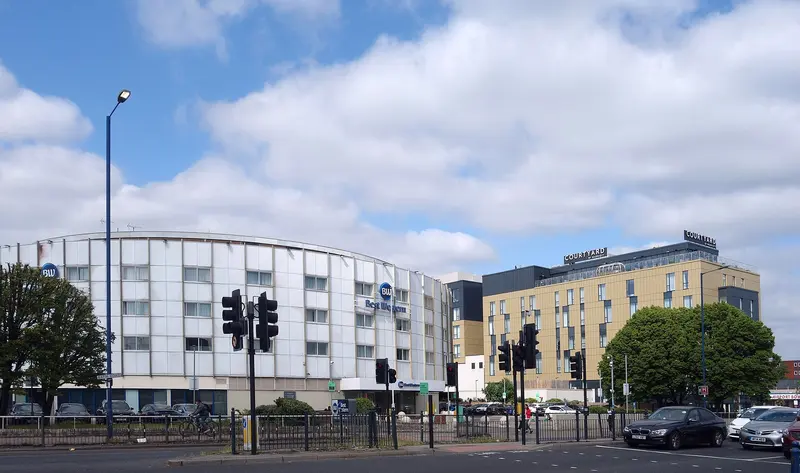 The round white Best Western hotel and the gold-clad Courtyard hotel beside traffic lights on the Bath Road under a blue sky.